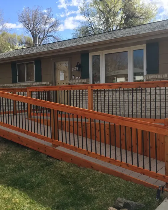 Composite ramp with stained cedar rails and black balusters along the front of a ranch house