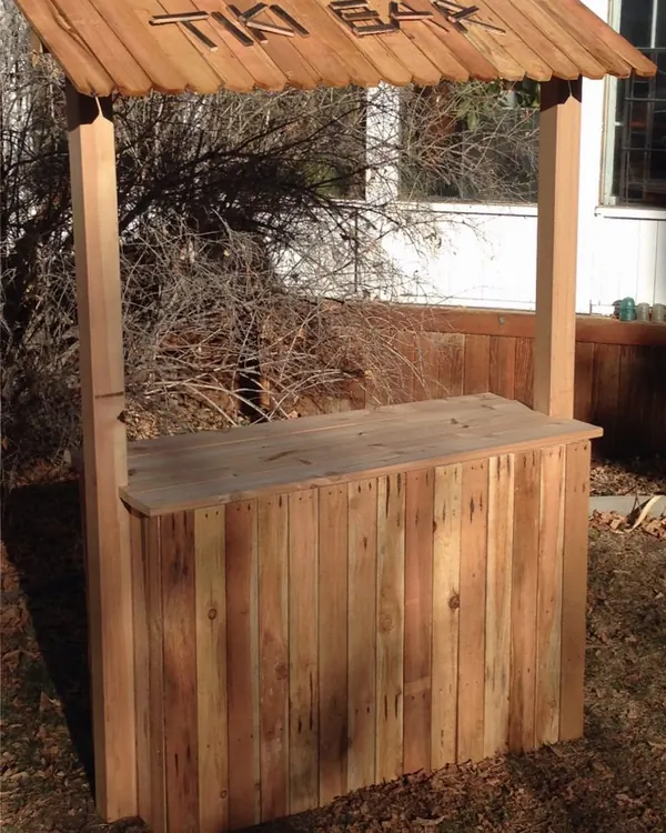 Cedar tiki bar with a carved Tiki Bar sign on its roof